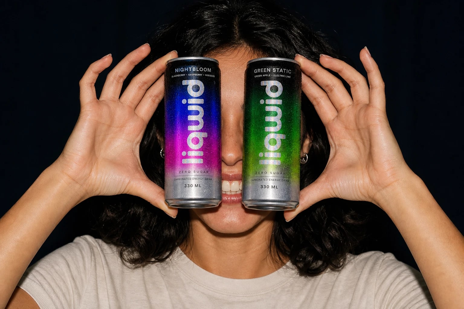 A smiling woman holding Nightbloom and Green Static cans playfully in front of her eyes.